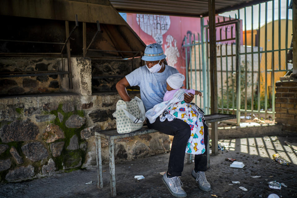 Stanley takes care of his 10-month-old daughter Ntokoso as his wife joins thousands who lined up to receive food handouts in the Olievenhoutbos township of Midrand, South Africa, Saturday May 2, 2020. though South Africa begun a phased easing of its strict lockdown measures on May 1, its confirmed cases of coronavirus continue to increase. (AP Photo/Jerome Delay)