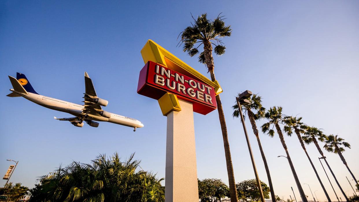 Los Angeles, USA - May 13, 2013: Airplane flying over In-n-Out Burger, LAX, few cars are leaving In-n-out parking lot.