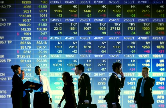 People standing in front of a display of stock prices.