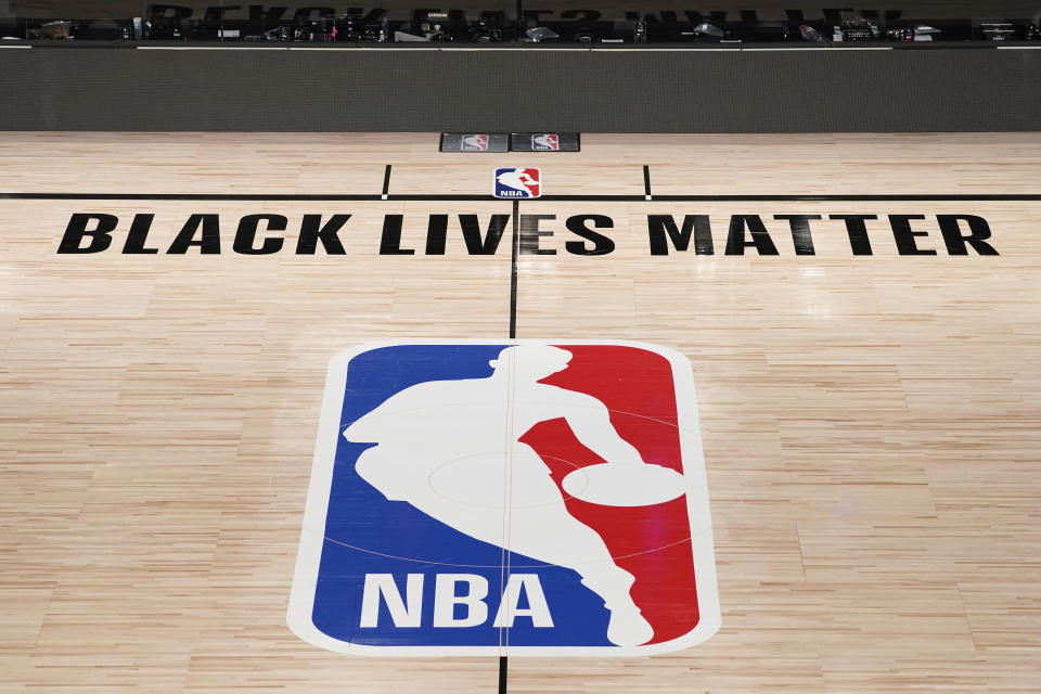 FILE- In this Aug. 28, 2020, file photo, Black Lives Matter is displayed near the NBA logo in an empty basketball arena in Lake Buena Vista, Fla. NBA training camps open around the league Tuesday, Dec. 1, 2020, though on-court sessions will be limited to individual workouts and only for those players who have gotten three negative coronavirus test results back in the last few days. (AP Photo/Ashley Landis, Pool, File)