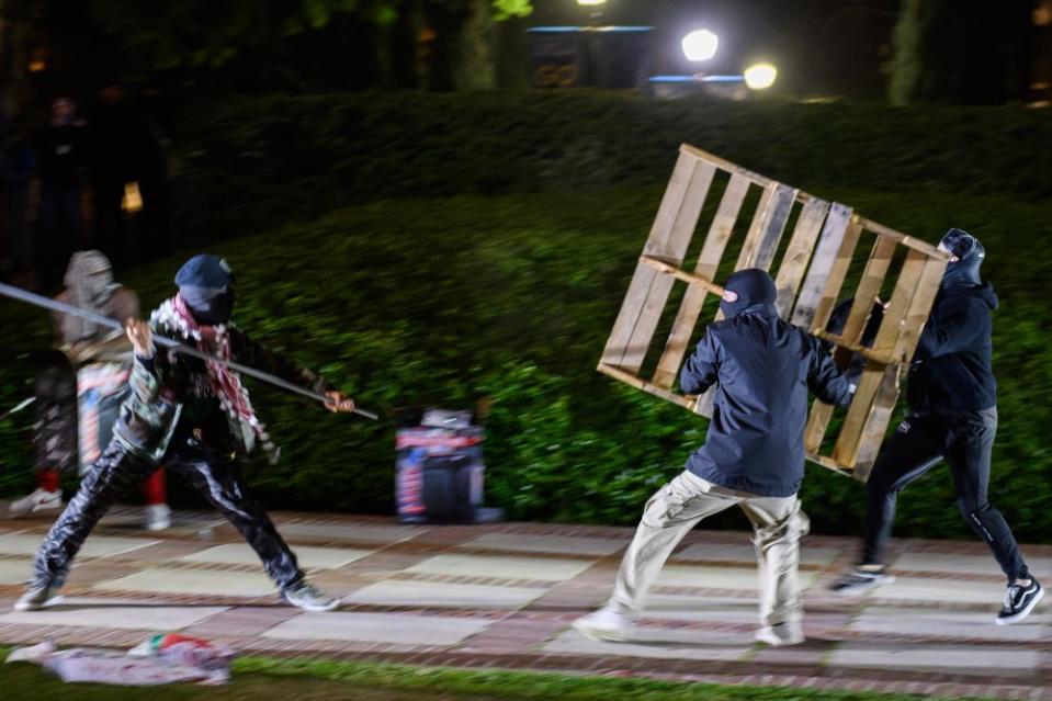 A Gaza solidarity encampment member and a counterprotester engage in a fight in Dickson Plaza on April 30. Throughout the night, counterprotesters tried to break through the metal barricades and wooden boards barricading one side of the encampment. Pieces of the debris, in the form of metal pipes, broken signs, and more, were used in fights that broke out.<span class="copyright">Zoraiz Irshad for The Daily Bruin</span>