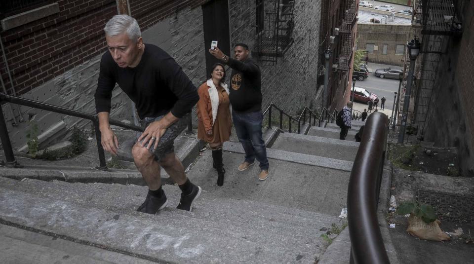 John Varela, left, climbs steps between two apartment buildings, Monday Oct. 28, 2019, in the Bronx borough of New York. The stairs have become a tourist attraction in recent weeks since the release of the movie “Joker.” In the movie, lead actor Joaquin Phoenix dances as he goes down the steps, wearing a bright red suit and clown makeup. Varela said after making pictures of his girlfriend on the stairs and seeing the movie, he "got the bug" to make the stairs part of his exercise routine. (AP Photo/Bebeto Matthews)
