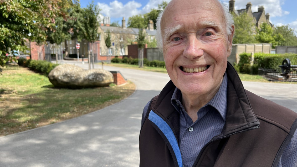 Jack Hayward smiles in a park with the railway village behind him and the DMJ tower in the distance