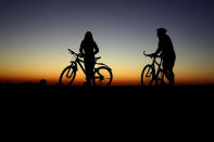 Cyclists watch the colorful sky waiting for the sunrise in Munich, Germany, Monday, April 6, 2020. Due to the coronavirus German police patrol to prevent gatherings of more than two people in public places. (AP Photo/Matthias Schrader)