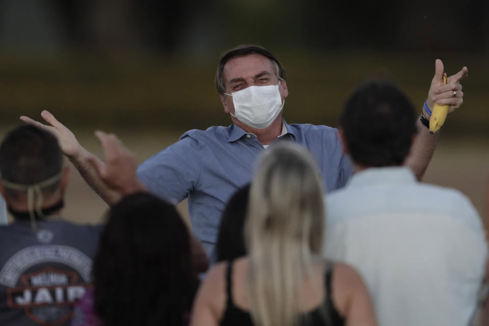 FILE - in this July 24, 2020 file photo, Brazil's President Jair Bolsonaro, who is infected with COVID-19, wears a protective face mask as he talks with supporters during a Brazilian flag retreat ceremony outside his official residence the Alvorada Palace, in Brasilia, Brazil. The South American nation proud of its role as a regional leader in science, technology and medicine, finds itself falling behind its neighbors in the global race for immunization against a pandemic that has already killed nearly 200,000 of its people. (AP Photo/Eraldo Peres, File)