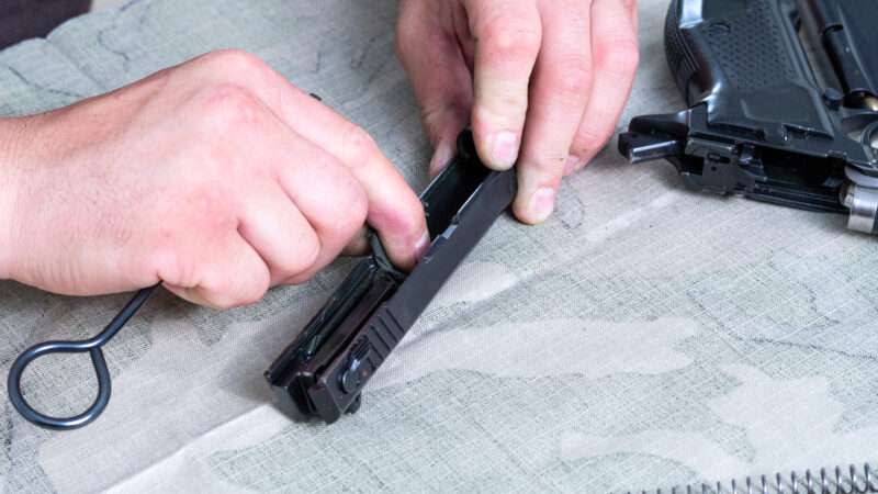 A man cleans the receiver of a disassembled handgun.