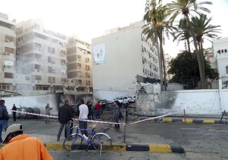 People and security stand at the scene of a car bomb explosion near the Egyptian embassy in the Libyan capital of Tripoli November 13, 2014. REUTERS/Stringer