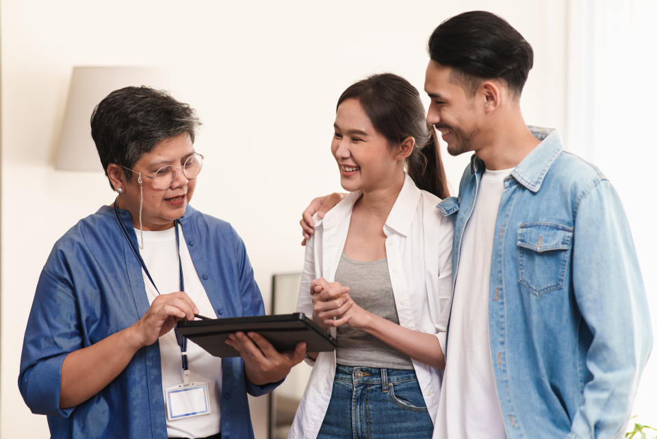 Senior woman real estate sales agent talking to a young Asian couple, illustrating a story on engaging a relative or friend as a property agent to sell your HDB or private home.