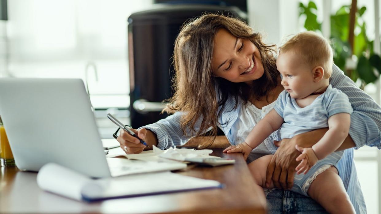 Young happy mother going through home finances and communicating with her baby son.