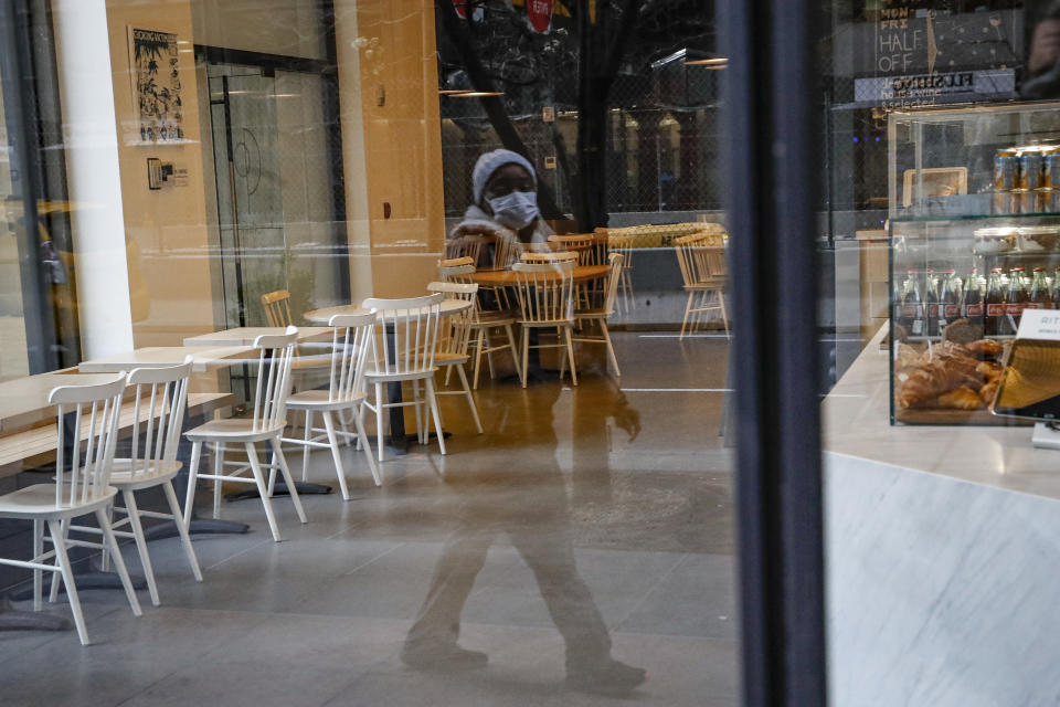 A pedestrian wearing a protective face mask walks past a nearly empty restaurant near Grand Central Terminal, Monday, March 16, 2020, in New York. New York leaders took a series of unprecedented steps Sunday to slow the spread of the coronavirus, including canceling schools and extinguishing most nightlife in New York City. (AP Photo/John Minchillo)