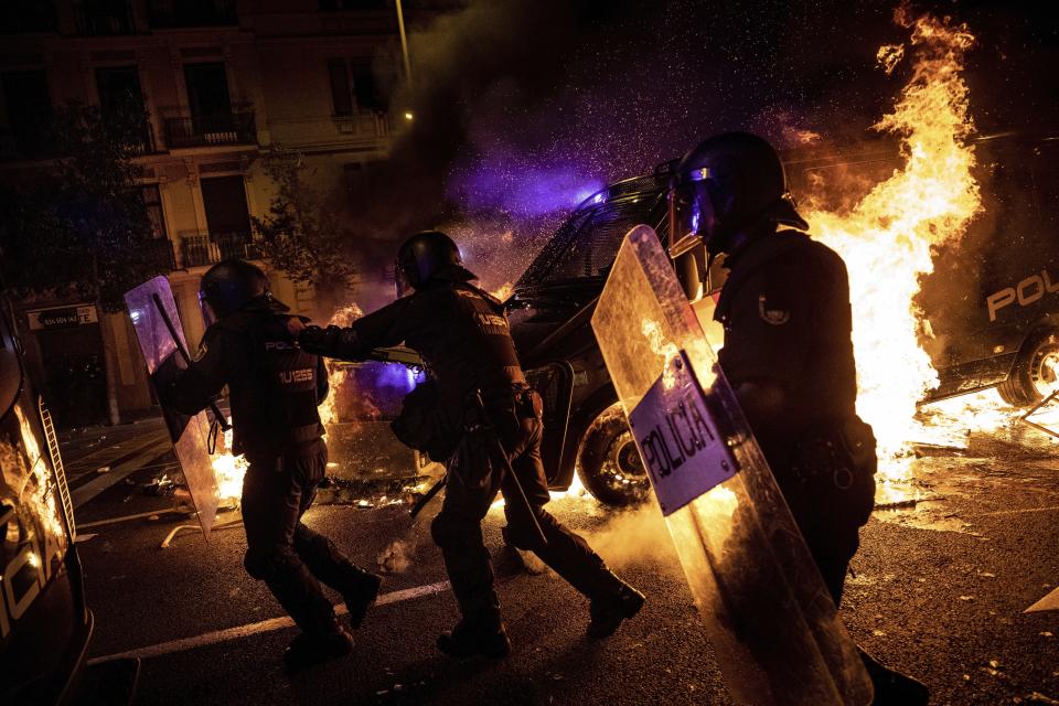 Policemen run as a police van drives over a burning barricade during clashes between protestors and police in Barcelona, Spain, Wednesday, Oct. 16, 2019. Spain's government said Wednesday it would do whatever it takes to stamp out violence in Catalonia, where clashes between regional independence supporters and police have injured more than 200 people in two days. (AP Photo/Bernat Armangue)