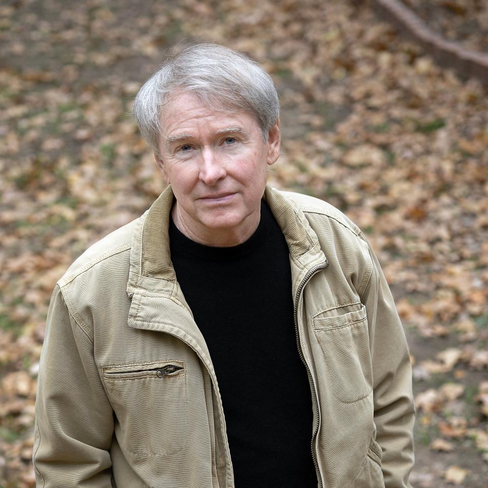A man in a jacket stands among fallen leaves.