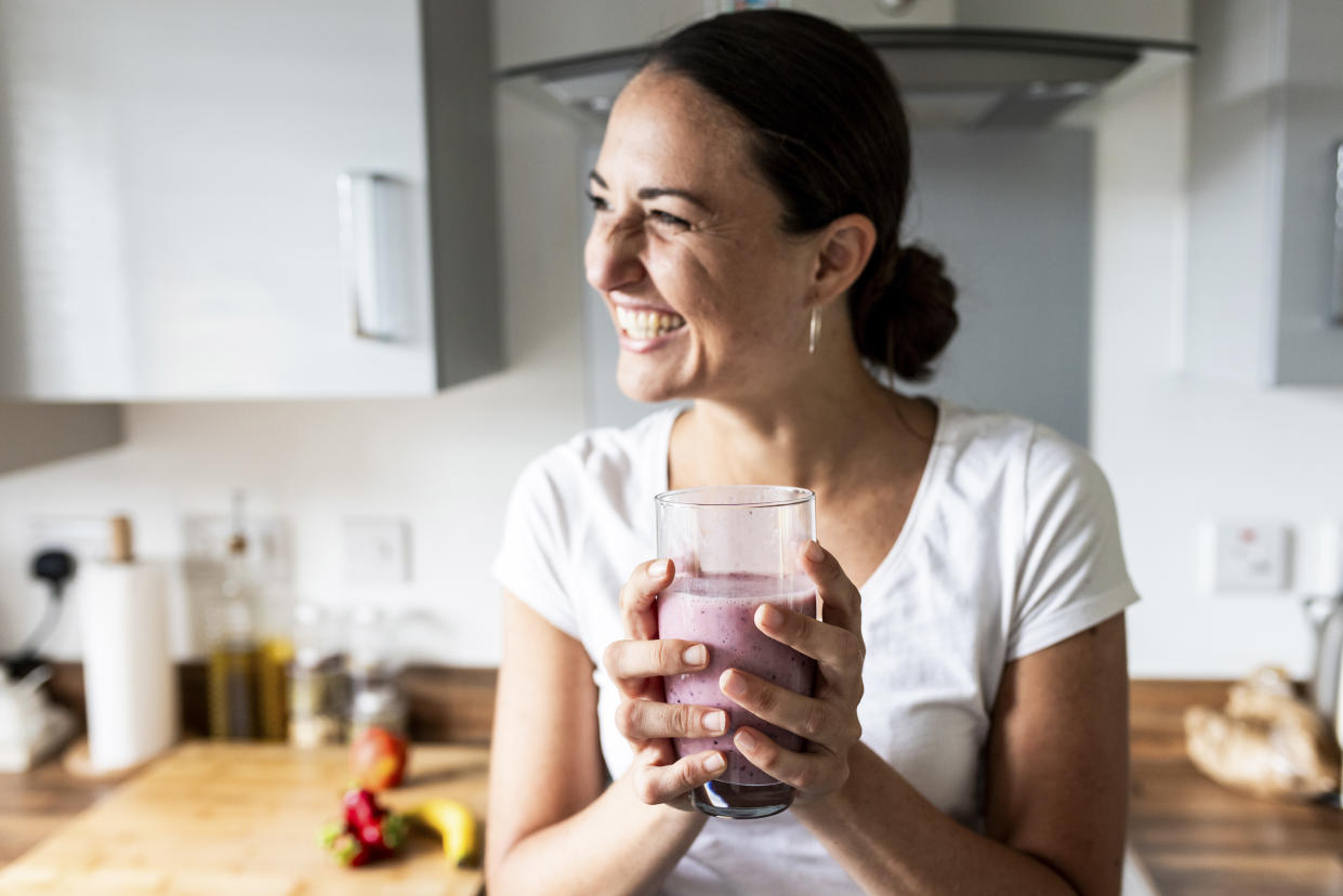 Cheerful woman holding glass of milkshake at home