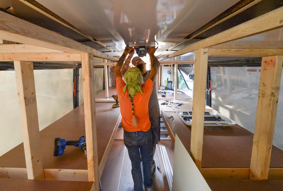 Kyle McNeil (front) and Anthony Rommel work on installing a light fixture inside a bus being converted to a mobile homeless shelter bus by the crew at The Source, on Wednesday, Jan. 17, 2023 in Indian River County. Anthony Zorbaugh, executive director of The Source, hopes to sell one to Rhode Island officials for an emergency-shelter pilot program.