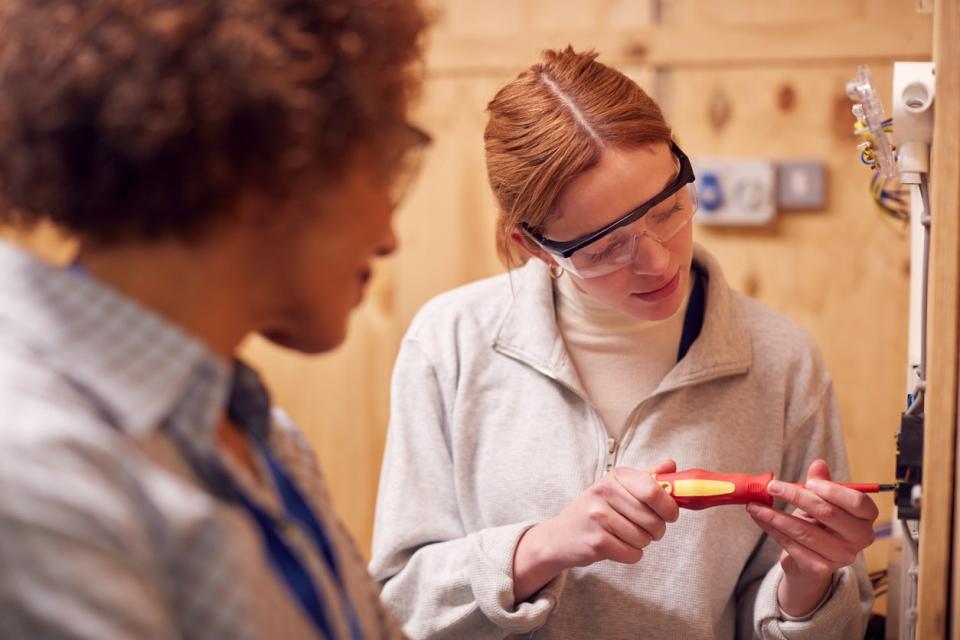 A woman uses an electrical tool while a colleague watches.