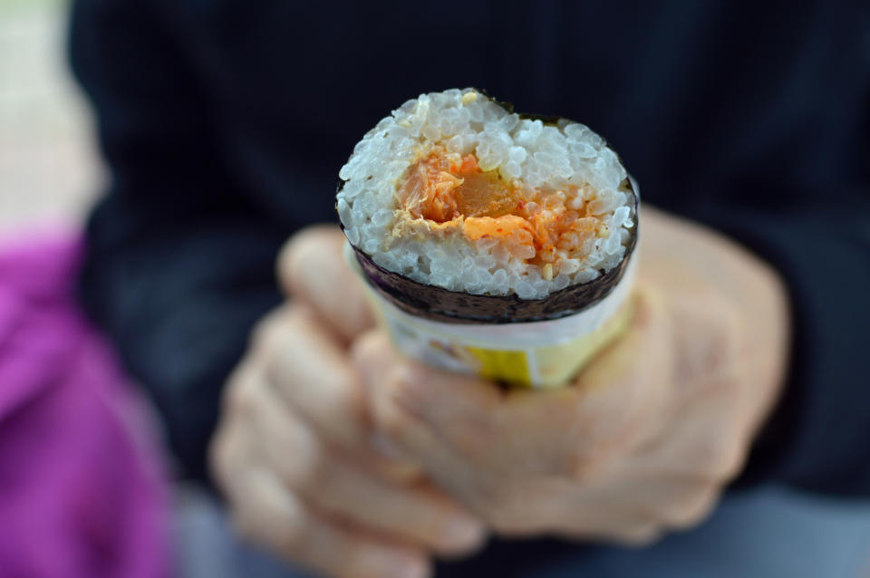 Person holding a sushi roll with visible rice and fillings