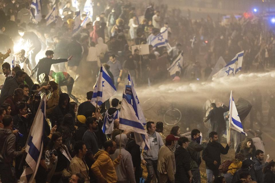 Israeli police use a water cannon to disperse demonstrators blocking a highway during a protest against plans by Prime Minister Benjamin Netanyahu's government to overhaul the judicial system in Tel Aviv, Israel, Monday, March 27, 2023. Tens of thousands of Israelis have poured into the streets across the country in a spontaneous outburst of anger after Prime Minister Benjamin Netanyahu abruptly fired his defense minister for challenging the Israeli leader's judicial overhaul plan. (AP Photo/Oren Ziv)