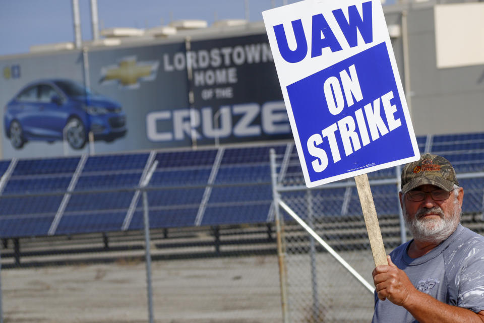 FILE - In this Sept. 16, 2019, file photo a picketer carries sign at one of the gates outside the closed General Motors automobile assembly plant in Lordstown, Ohio. Many from Lordstown, Ohio, and near Baltimore and Detroit are opposing a deal that could end a 37-day strike that crippled GM’s U.S. production and cost the company an estimated $2 billion. (AP Photo/Keith Srakocic, File)