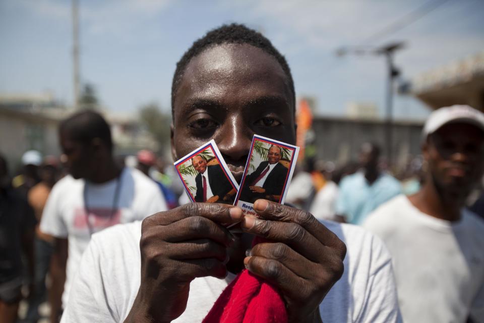 A demonstrator holds up pictures of Haiti's former President Jean-Bertrand Aristide during rally to mark the tenth anniversary of his second ouster in Port-au-Prince, Haiti, Thursday, Feb. 27, 2014. The protesters denounced what they described as widespread corruption in the government of President Michel Martelly and even called for his resignation. (AP Photo/Dieu Nalio Chery)