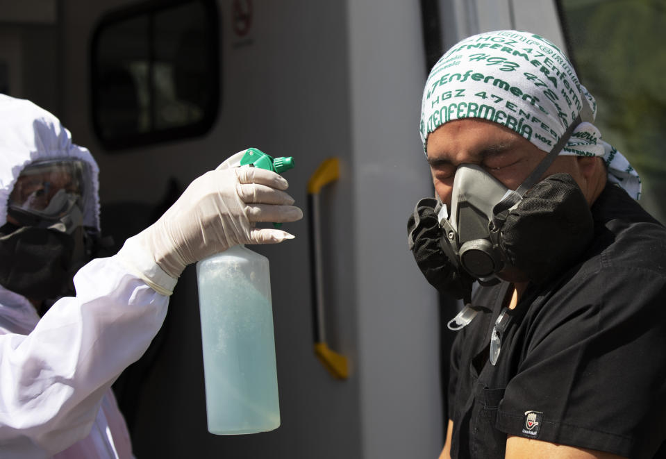 Paramedics Carolina Estrada, left, disinfects her partner Elvin Munguia after mobilizing a COVID-19 patient from his home to a hospital in the Iztapalapa district of Mexico City, Tuesday, Feb. 2, 2021. (AP Photo/Marco Ugarte)