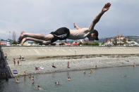 A boy flies over water as other people enjoy the beach in the Black Sea resort of Sochi, Russia, Sunday, July 5, 2020. Tens of thousands of vacation-goers in Russia and Ukraine have descended on Black Sea beaches, paying little attention to safety measures despite levels of contagion still remaining high in both countries. (AP Photo/Artur Lebedev)