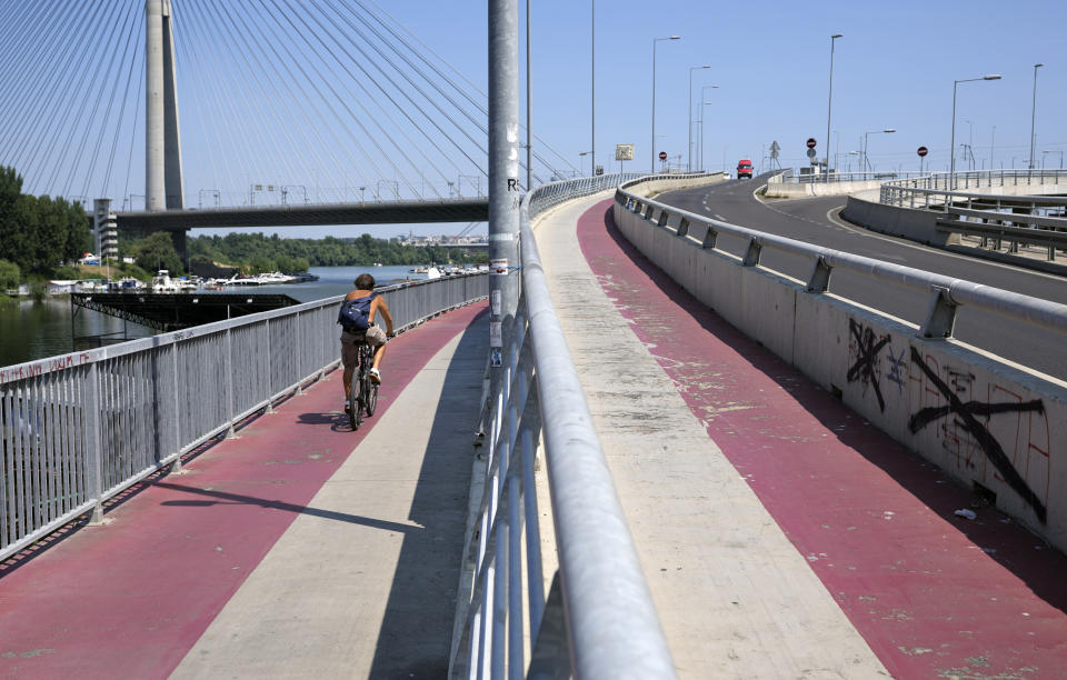 A man rides a bicycle on Ada bridge over the Sava river in Belgrade, Serbia, Friday, Aug. 13, 2021. More intense heat baked Italy, Spain and Portugal on Friday, with even higher temperatures looming in weekend forecasts. In Serbia, the army has deployed water tanks and authorities have appealed on the residents to avoid watering their gardens. (AP Photo/Darko Vojinovic)