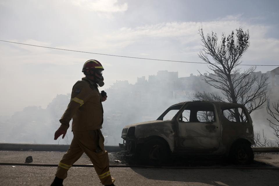 A firefighter walks next to a burnt car during a wildfire in Voula suburb, in southern Athens, Greece, Saturday, June 4, 2022. A combination of hot, dry weather and strong winds makes Greece vulnerable to wildfire outbreaks every summer. (AP Photo/Yorgos Karahalis)