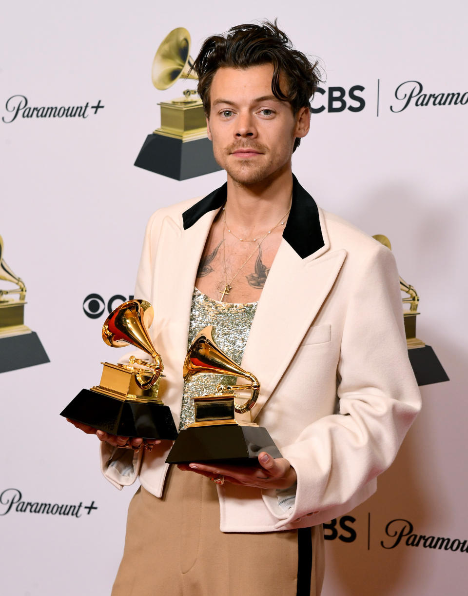 his chest tattoos are showing above his shirt and he's holding two awards