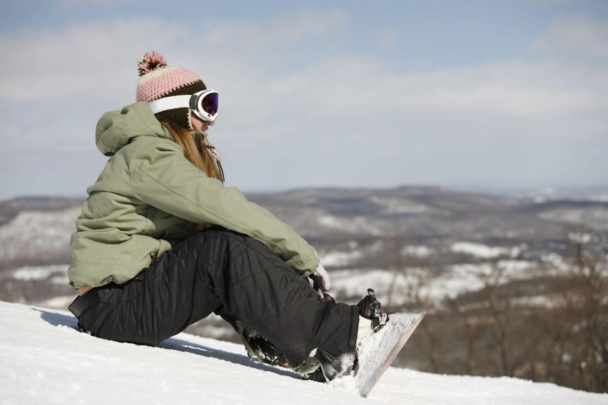 woman sitting on ski slope with snowboard and snow pants