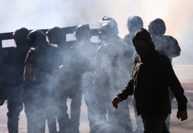 A man walks next to police officers among tear gas during a protest against Brazilian President Jair Bolsonaro in Sao Paulo