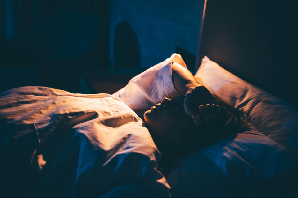 Person lying in bed with hands over forehead, appearing stressed or unable to sleep