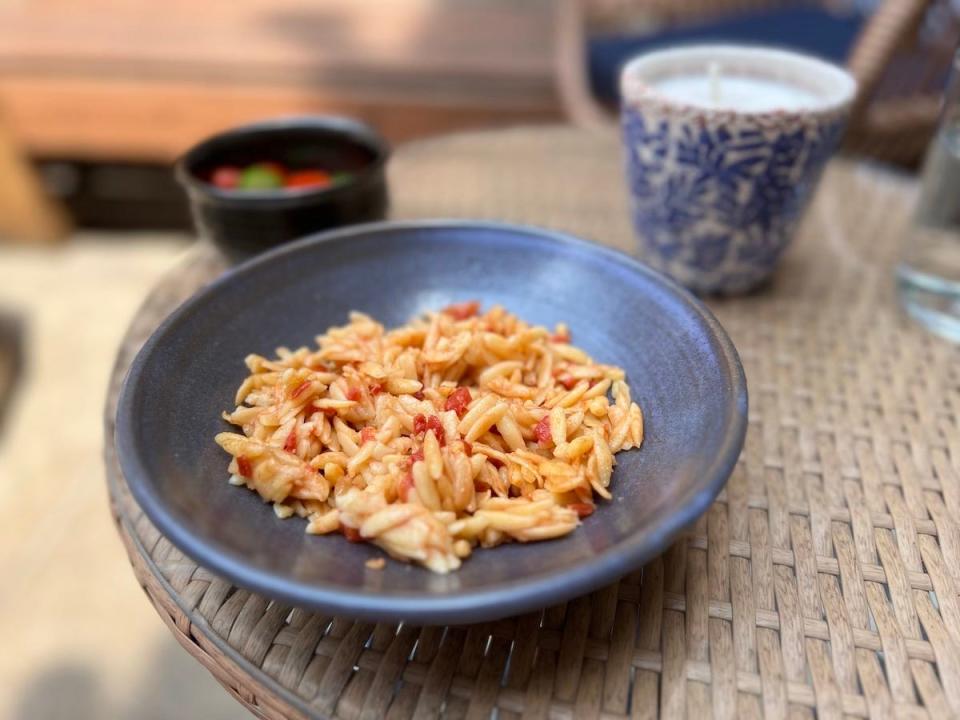 A bowl of kritharaki, a Greek tomato-orzo dish, on a table outside.