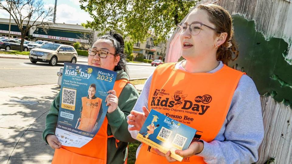 Haylee McFall, a la derecha, y Rose Xiong, estudiantes de odontología de Fresno State, reparten postales del Kids Day con códigos QR a los automovilistas que pasan, para que hagan donaciones al Kids Day anual a beneficio del Hospital Infantil Valley, cerca de Fresno State, el martes 7 de marzo de 2023.