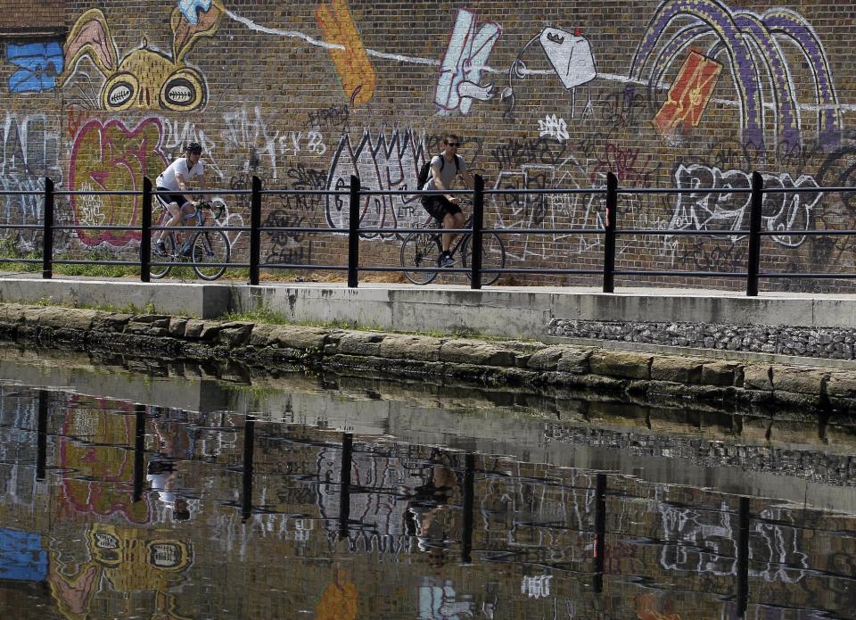 Cyclists ride past colourful graffiti on a canal side cycle path in London, Thursday, May 24, 2012. There are many cycle paths across London that can be used to travel the capital. Like a runner or a swimmer, you would need to be physically fit. Like a goalie or a boxer, you should be prepared for close calls. But if you are coming to London's Summer Olympics _ and you have what it takes _ using a bicycle could be a great option in a city bracing for gridlock. (AP Photo/Kirsty Wigglesworth)