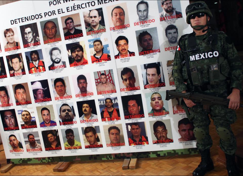 An army soldier stands next to a banner displaying mug shots of persons detained or killed by the Mexican Army during the media presentation of Daniel Ramirez, alias "El Loco", not pictured, in Mexico City, Monday, May 21, 2012. Ramirez is believed to be a member of the Zetas drug cartel allegedly involved in the dumping of more than 40 hacked-up bodies on a highway outside the city of Cadereyta near Monterrey. The bodies with their heads, hands and feet hacked off were found May 13. (AP Photo/Alexandre Meneghini)