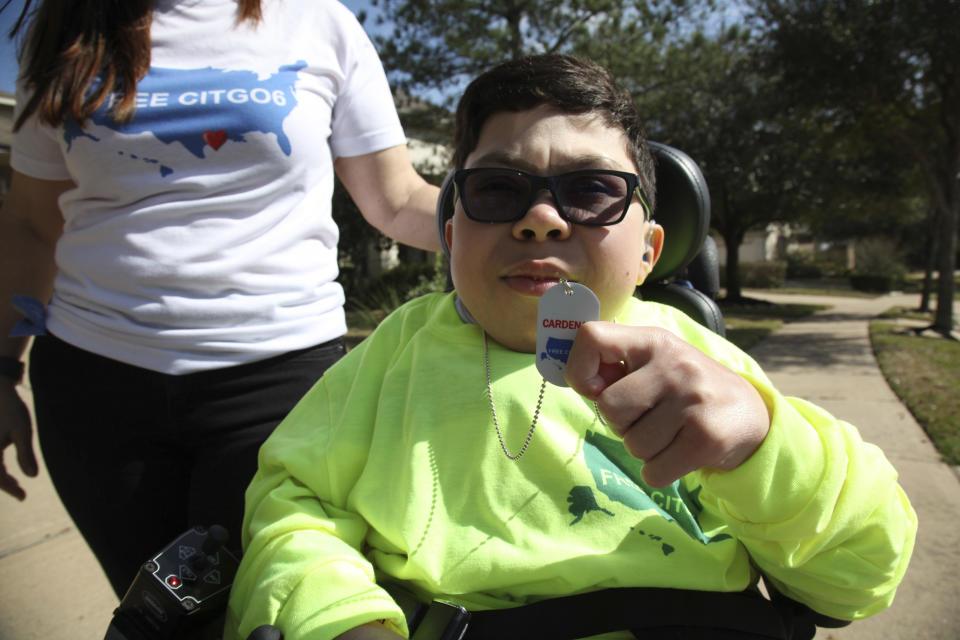 Sergio Cardenas, whose father Gustavo is being held in a Venezuelan jail along with five other Citgo executives since November 2017, holds a necklace emblazoned with a logo "Free the Citgo 6," as he poses for a photo outside his home in Katy, Texas, Friday, Feb. 15, 2019. Sergio, who suffers from a rare metabolic disease called mucolipidosis that stunted his physical growth, visited his father for two hours at a Caracas jail, after he was taken there by his mother who fears their son could die before his father’s release. (AP Photo/John L Mone)