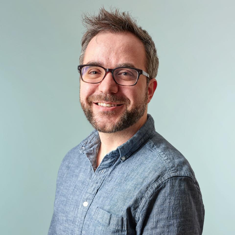 Headshot of Adam wearing a blue button up shirt on a white background