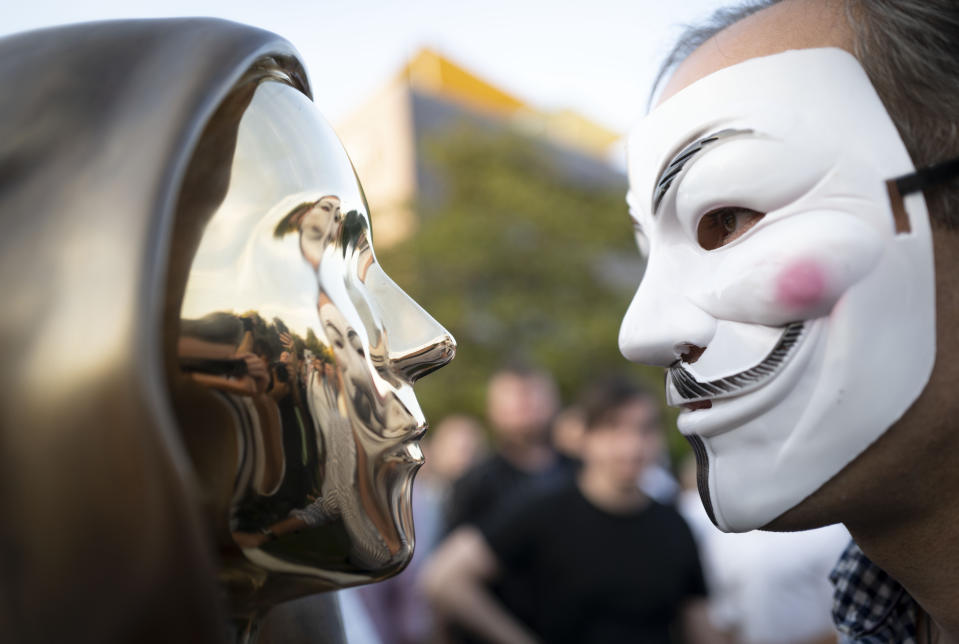 A man wearing a a Guy Fawkes mask looks at a newly unveiled statue of the mysterious developer of the Bitcoin digital currency in Budapest, Hungary, Thursday, Sept. 16, 2021. A bronze statue was unveiled in Hungary’s capital on Thursday which its creators say is the first in the world to pay homage to the anonymous creator of the Bitcoin digital currency. Erected in a business park near the Danube River in Budapest, the bust sits atop a stone plinth engraved with the name of Satoshi Nakamoto, the pseudonym of the mysterious developer of Bitcoin whose true identity is unknown. (AP Photo/Bela Szandelszky)