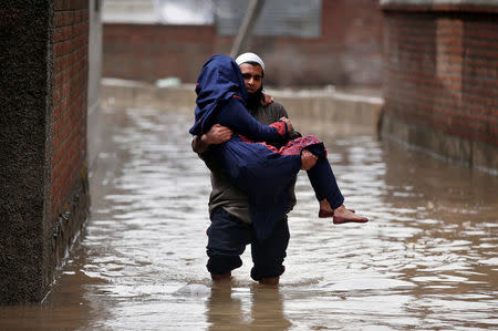 A man carries a woman as he wades through a flooded street after incessant rains in Srinagar April 7, 2017. REUTERS/Danish Ismail