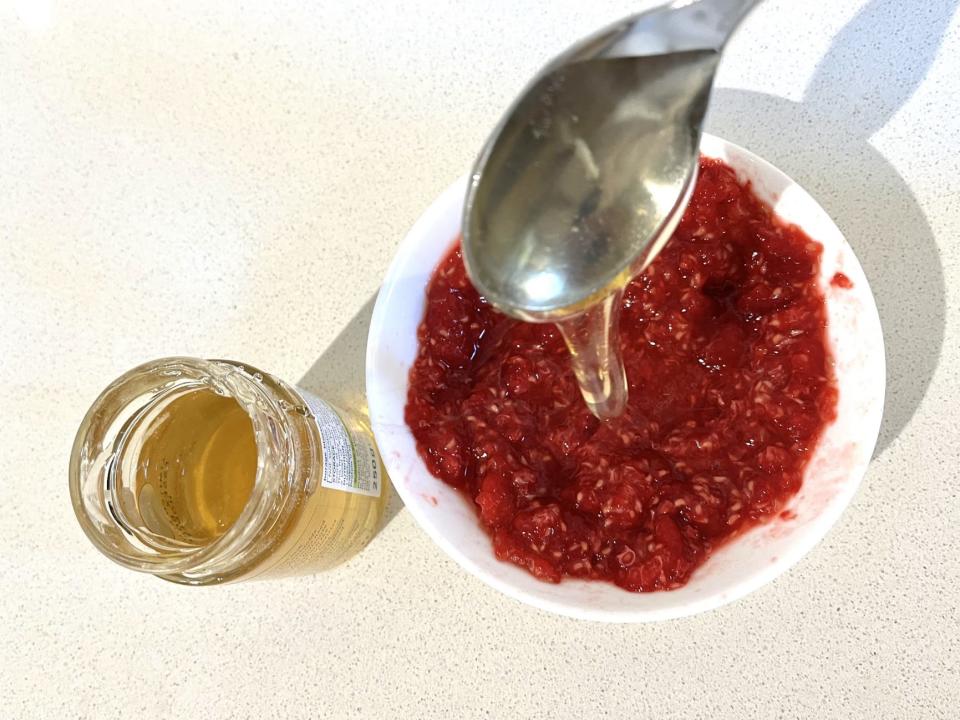 Honey being poured into a bowl of crushed raspberries.