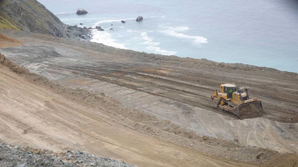 Bulldozer pushes and compacts dirt for a fill area below the highway grade at the edge of the Pacific Ocean. Crews from Papich Construction Co. work on Paul’s Slide on Highway 1 north of Gorda on May 17, 2024. Repairs are expected to be completed this summer.