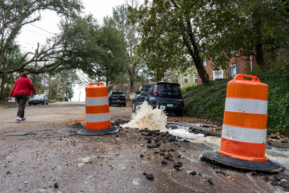 A woman walks past as water from an apparent burst water pipe bubbles a constant stream of water on Quinn Street on Saturday, Jan. 8, 2022.