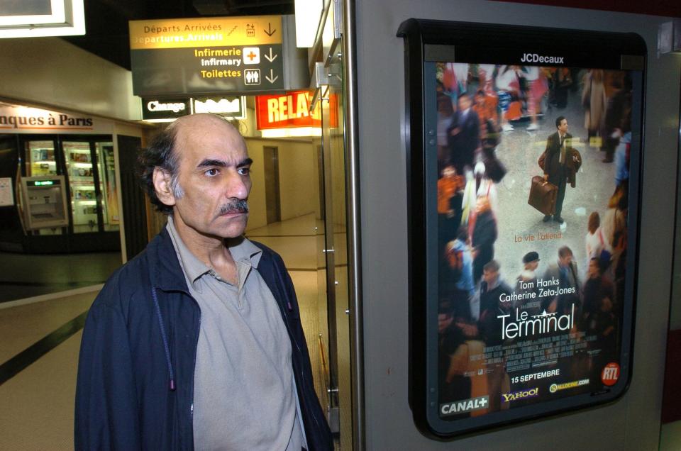 (FILES) In this file photo taken on August 12, 2004 Mehran Karimi Nasseri passes by the poster of the movie inspired by his life, in the terminal 1 of Paris Charles De Gaulle airport. - Mehran Karimi Nasseri, a political refugee who lived over 18 years in Paris' Roissy-Charles de Gaulle airport and inspired director Steven Spielberg's "The Terminal", died, aged 77, at Roissy-Charles de Gaulle airport's terminal 2F, as reported to AFP by airport officials.