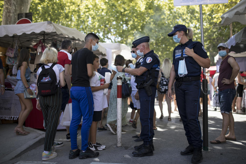 Municipal police give facemasks to pedestrians in Saint-Tropez, southern France, Saturday Aug 8, 2020. The glamorous French Riviera resort of Saint-Tropez is requiring face masks outdoors starting Saturday, threatening to sober the mood in a place renowned for high-end, free-wheeling summer beach parties. (AP Photo/Daniel Cole)