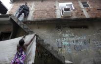 A woman extends a sheet on a clothesline as police officer patrols during an operation at the Mare slums complex in Rio de Janeiro March 25, 2014. Brazil will deploy federal troops to Rio de Janeiro to help quell a surge in violent crime following attacks by drug traffickers on police posts in three slums on the north side of the city, government officials said on Friday. Less than three months before Rio welcomes tens of thousands of foreign soccer fans for the World Cup, the attacks cast new doubts on government efforts to expel gangs from slums using a strong police presence. The city will host the Olympics in 2016. REUTERS/Ricardo Moraes (BRAZIL - Tags: CRIME LAW)