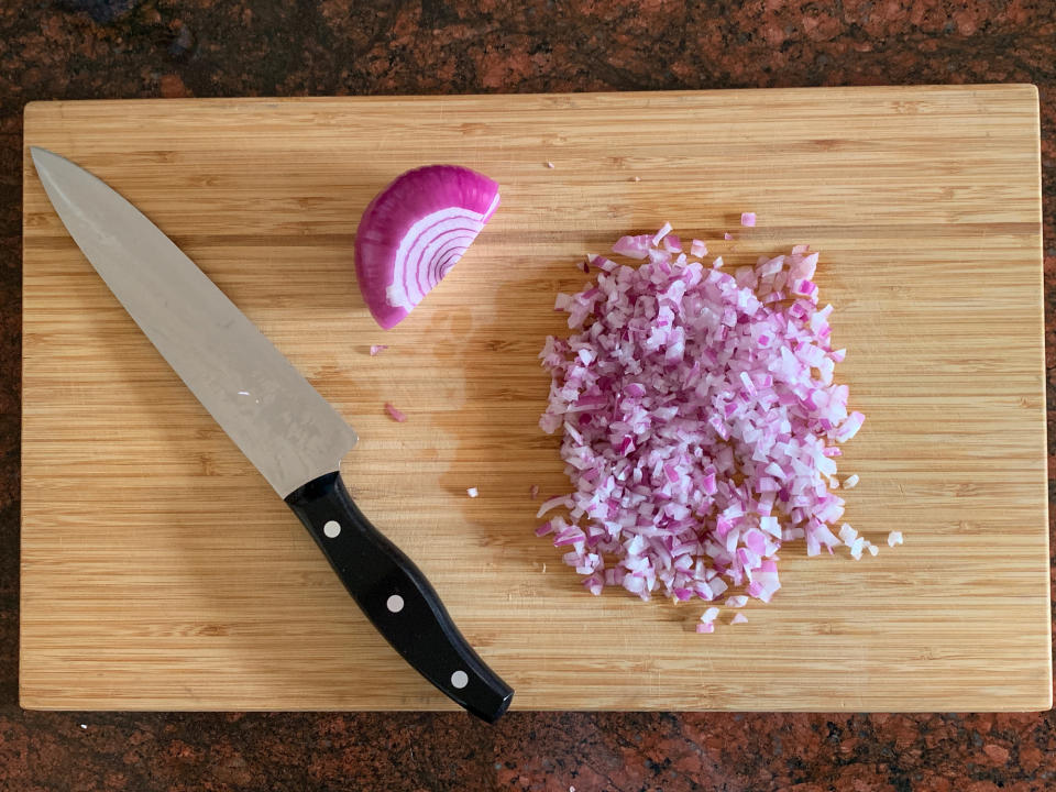 Finely diced red onion on a cutting board with kitchen knife.