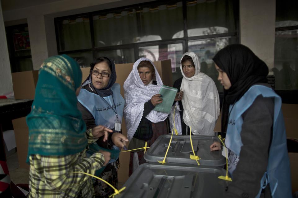 An Afghan election worker, second left, explains the process of elections to voters at a polling station in Kabul, Afghanistan, Saturday, April 5, 2014. Afghan voters lined up for blocks at polling stations nationwide on Saturday, defying a threat of violence by the Taliban to cast ballots in what promises to be the nation's first democratic transfer of power. Partial results are expected as soon as Sunday. (AP Photo/Muhammed Muheisen)