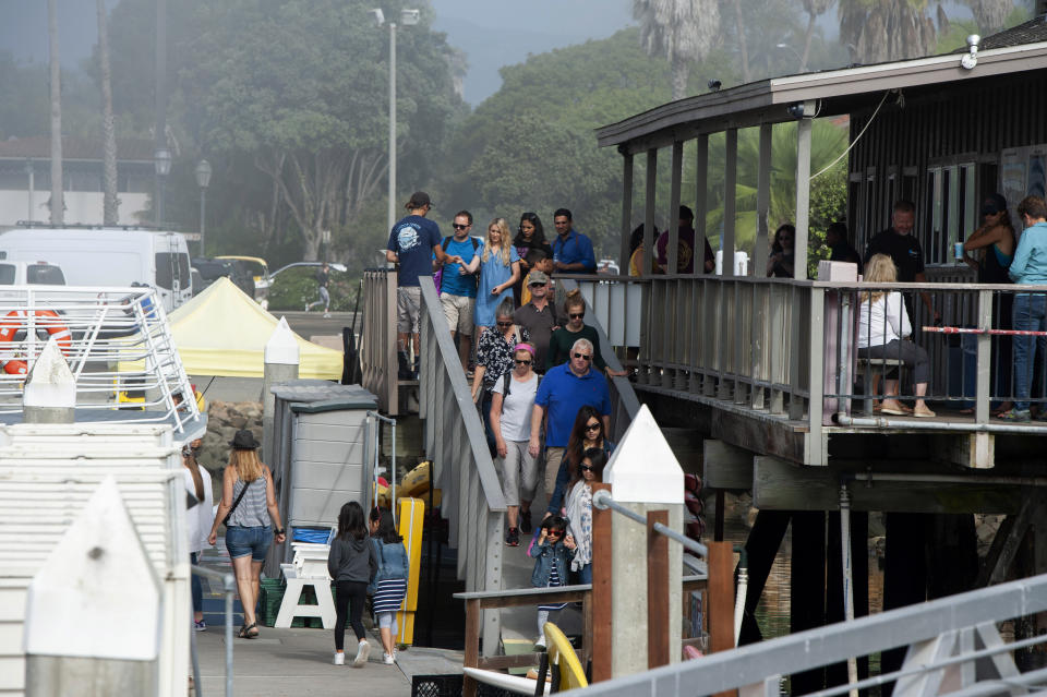 Whale watchers board a boat outside of the Truth Aquatics office in Santa Barbara, Calif., as people nearby await to hear news about a diving boat that caught fire and sank on Monday, Sept. 2, 2019. (AP Photo/Christian Monterrosa)