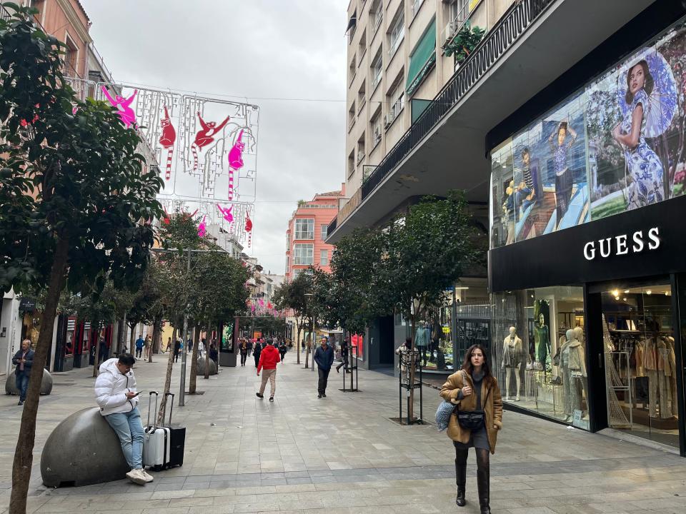 Pedestrians walking down street by shops in Madrid.