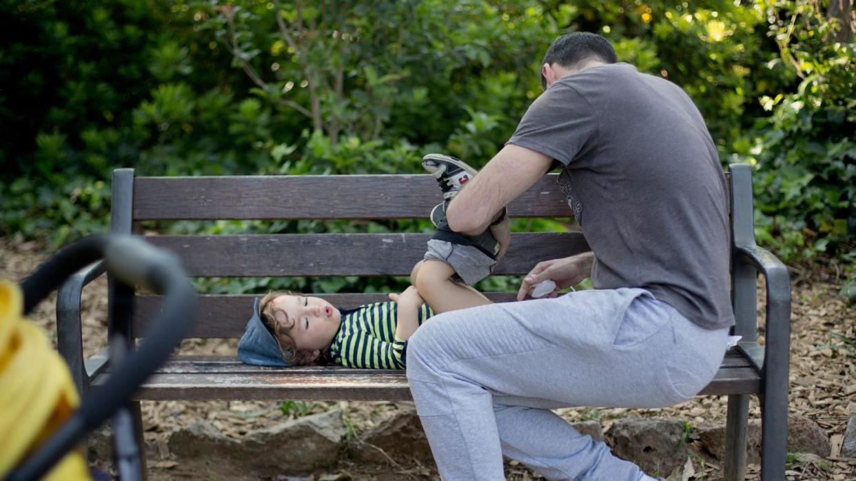 A dad changing a child's nappy on a park bench